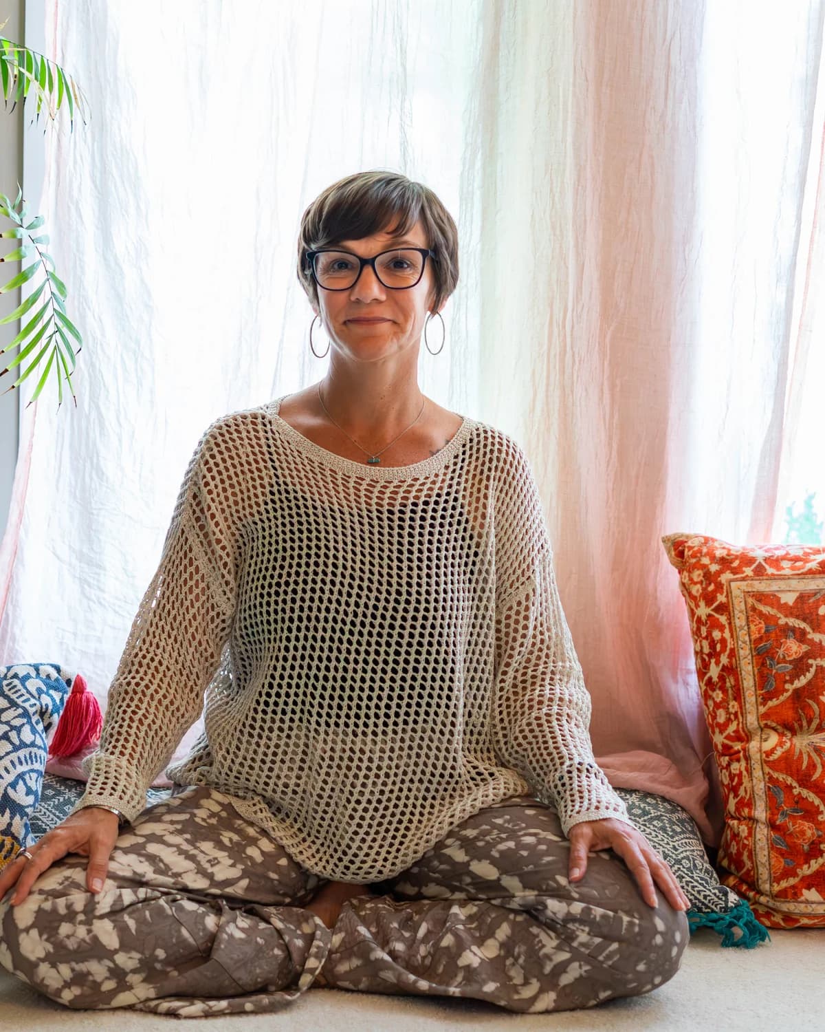 Nicole Domenic seated cross-legged on cushions by a sunlit window