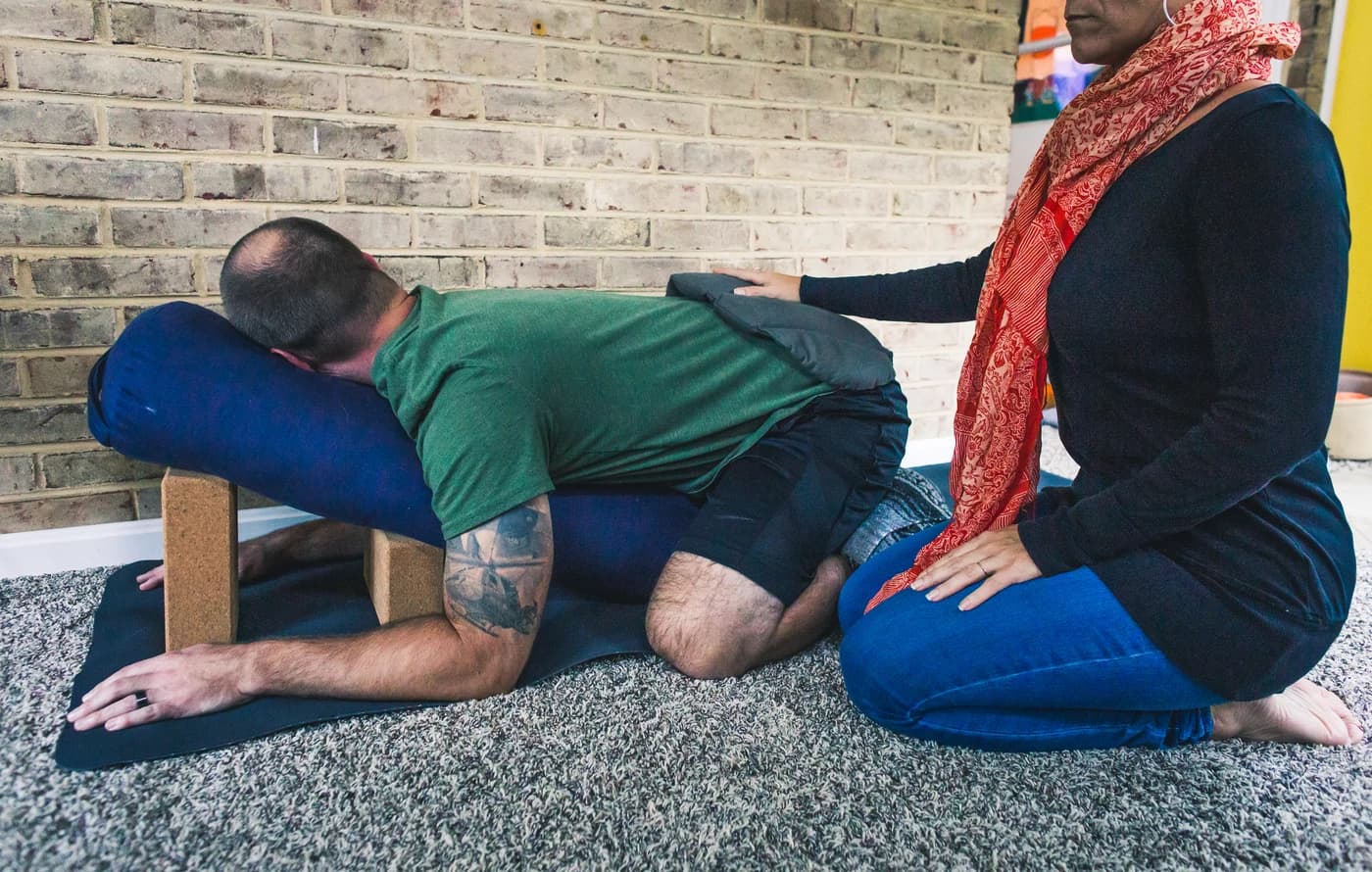 Nicole guiding a private yoga session, supporting a student resting over a bolster on blocks