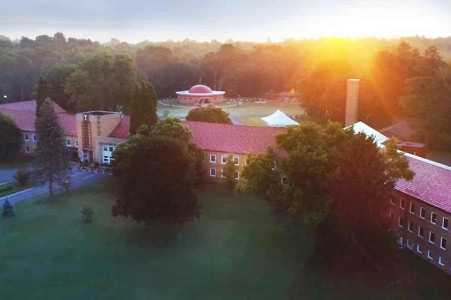Aerial view of the Himalayan Institute campus at sunrise, with the domed temple beyond the main building