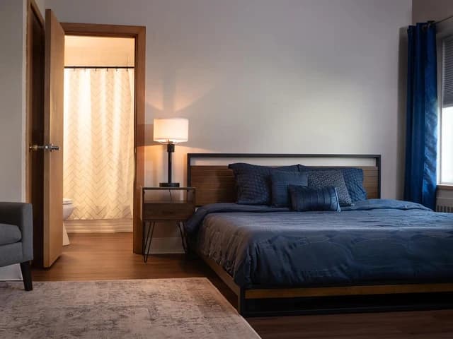 The Jivana Suite bedroom with a king bed in navy bedding and the en suite bathroom beyond