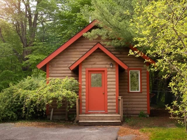 The Ananda Cottage, a small log cabin with a red door among trees