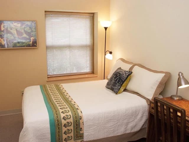 A private standard room with a made bed, a lamp, and a desk